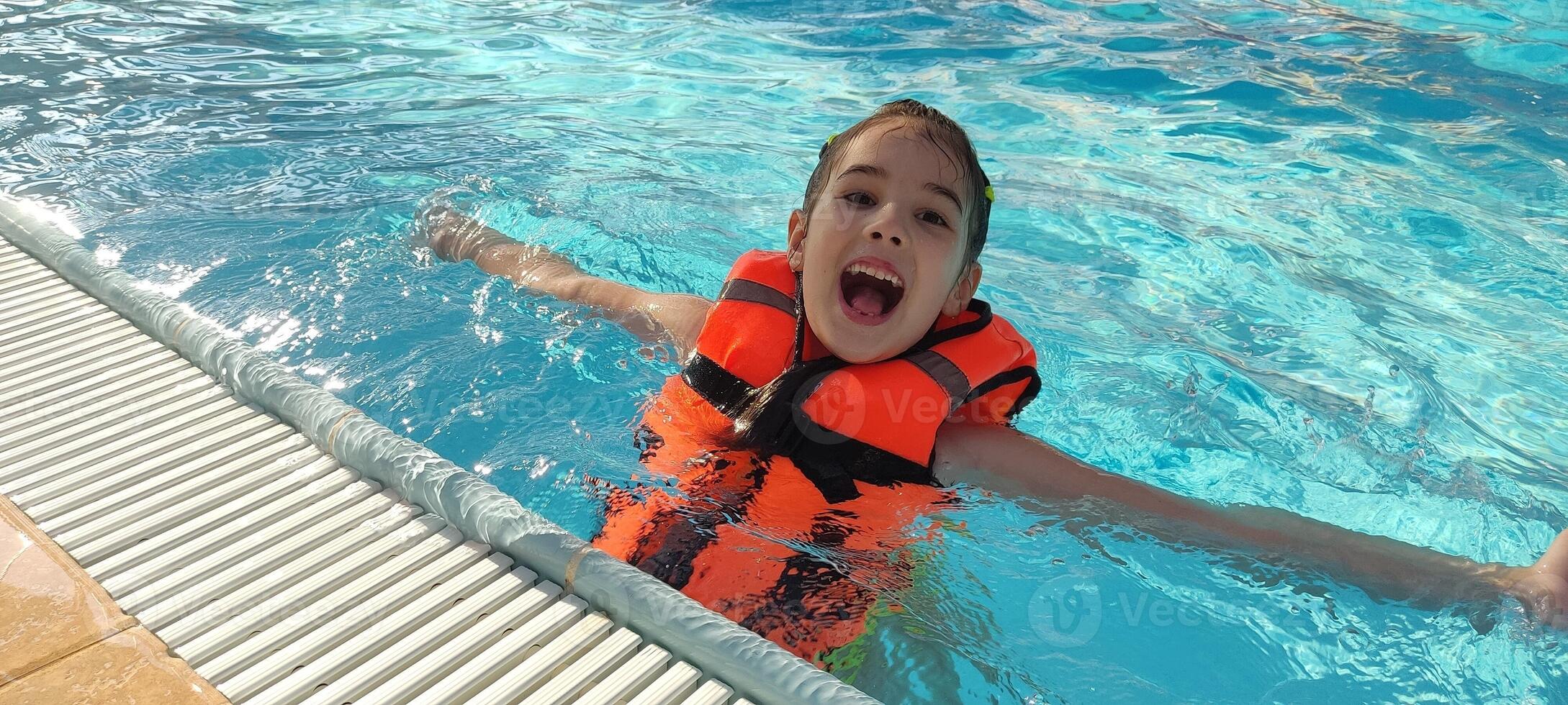 Joyful child swimming in pool wearing orange safety vest photo