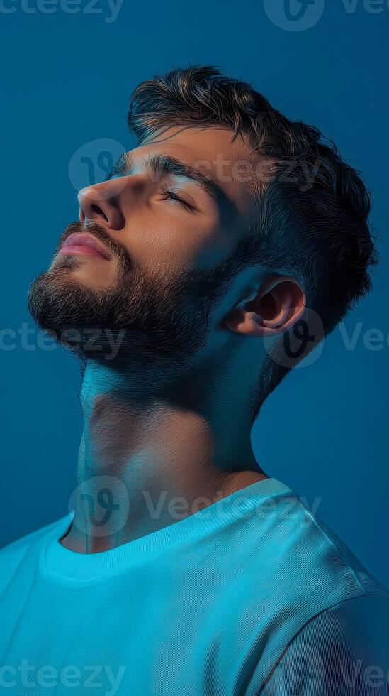 Young man expressing tranquility with closed eyes against a serene blue background, capturing a moment of introspection photo