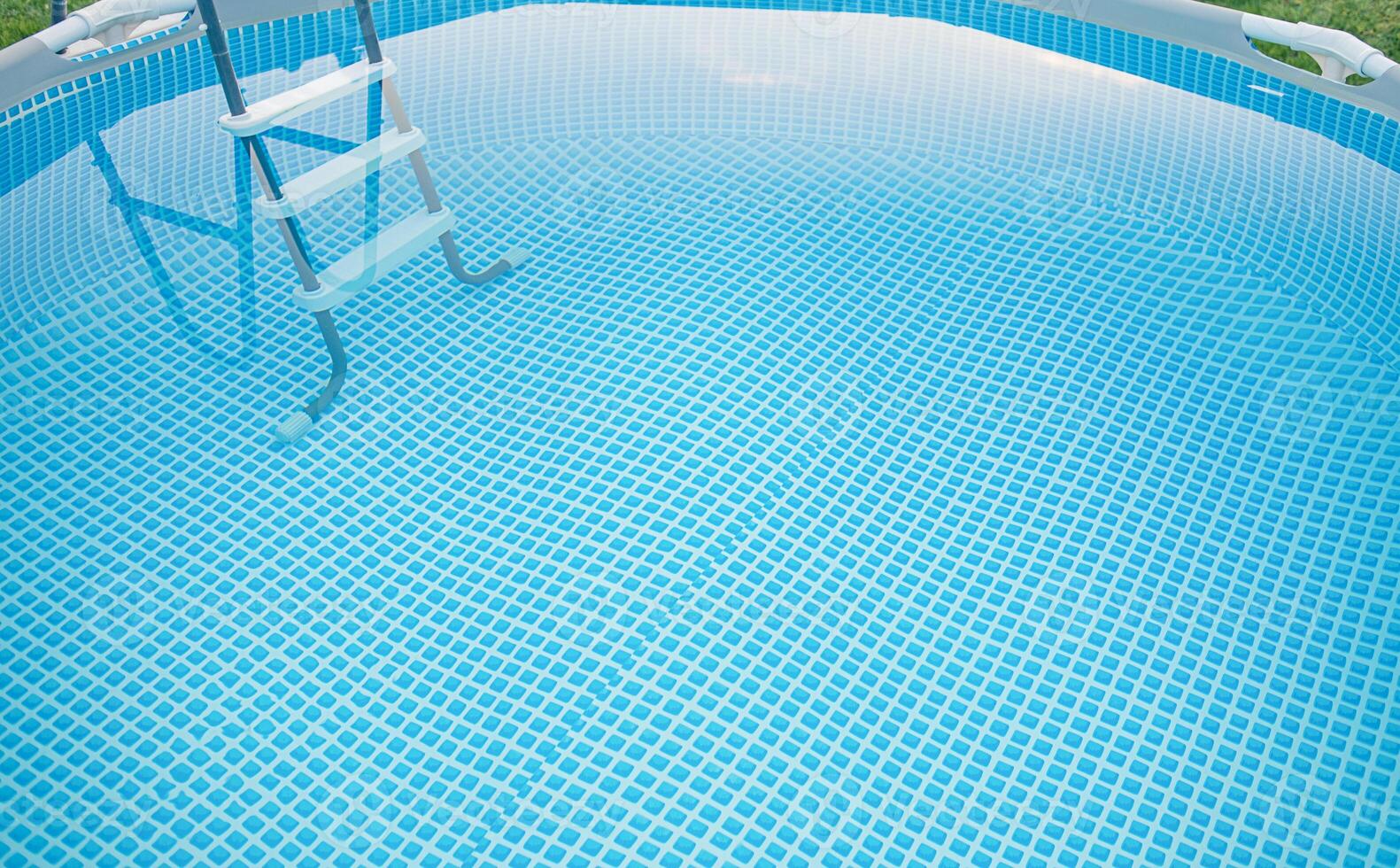 Frame pool with clean water for swimming and a ladder on the grass in summer. photo