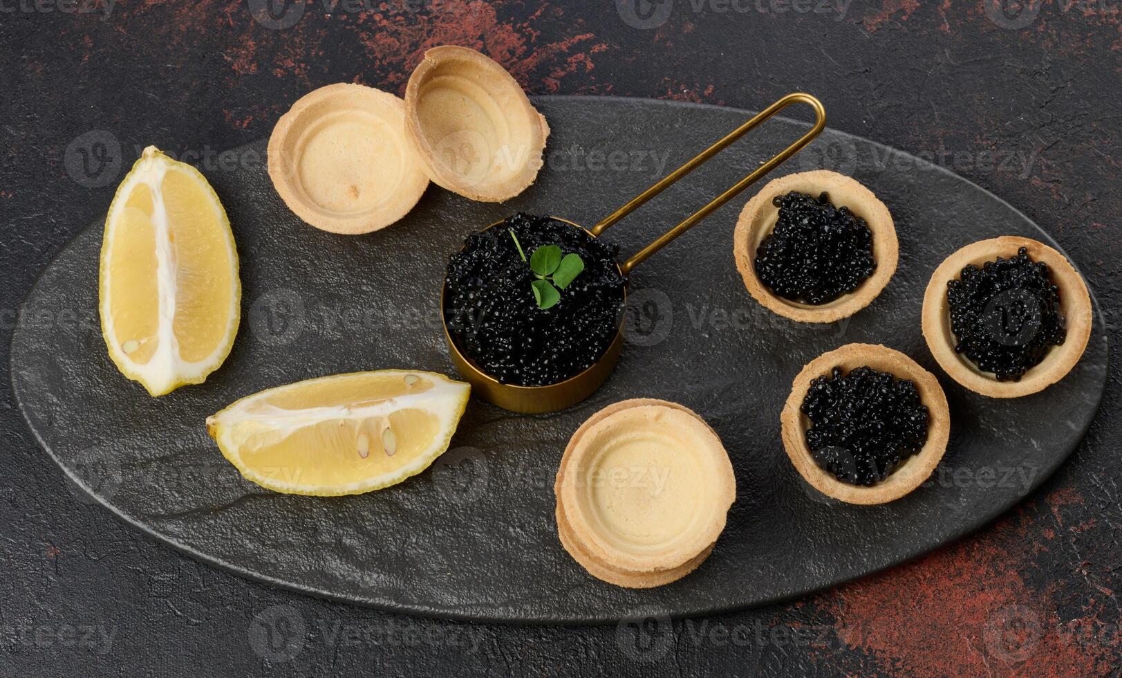 Black sturgeon caviar and empty round tartlets on table, top view. photo