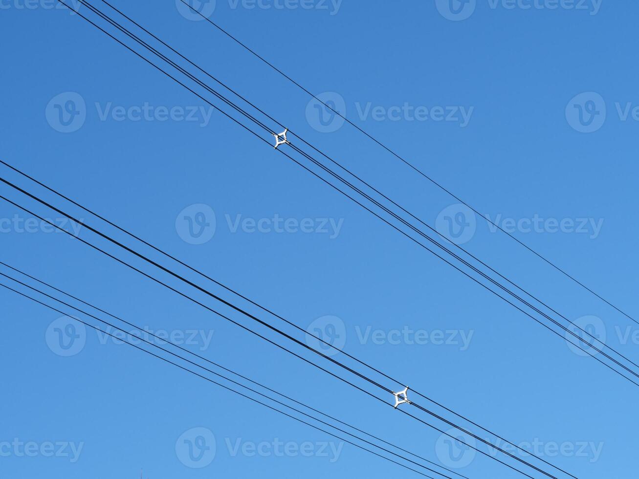 Overhead power cables with spacers against a blue sky photo