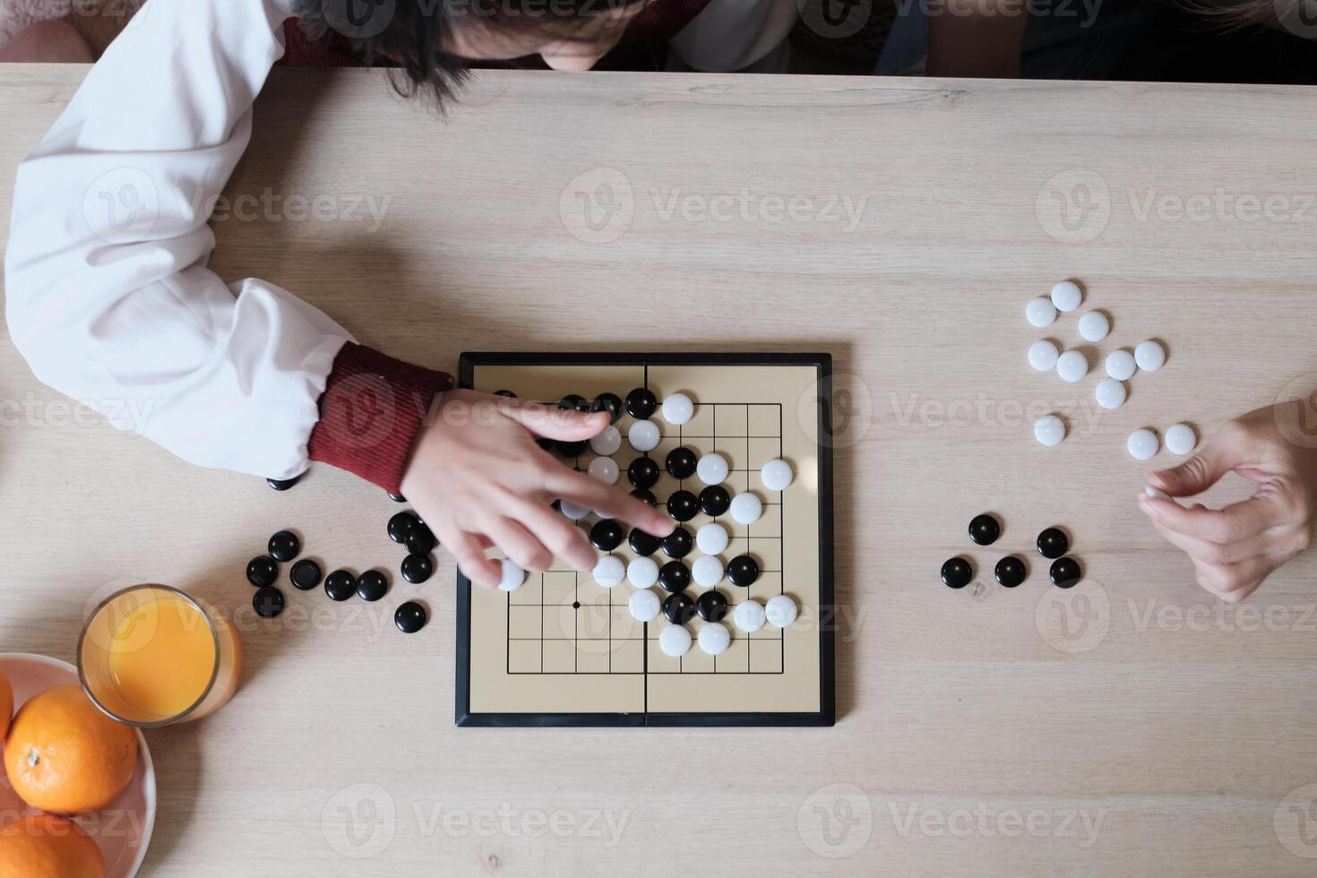 Close-up and top-view shots of GO, oriental checkers board game on wooden table are played by two Asian players, leisure time hobby, strategy decision and tactic challenge with compete concentrate. photo