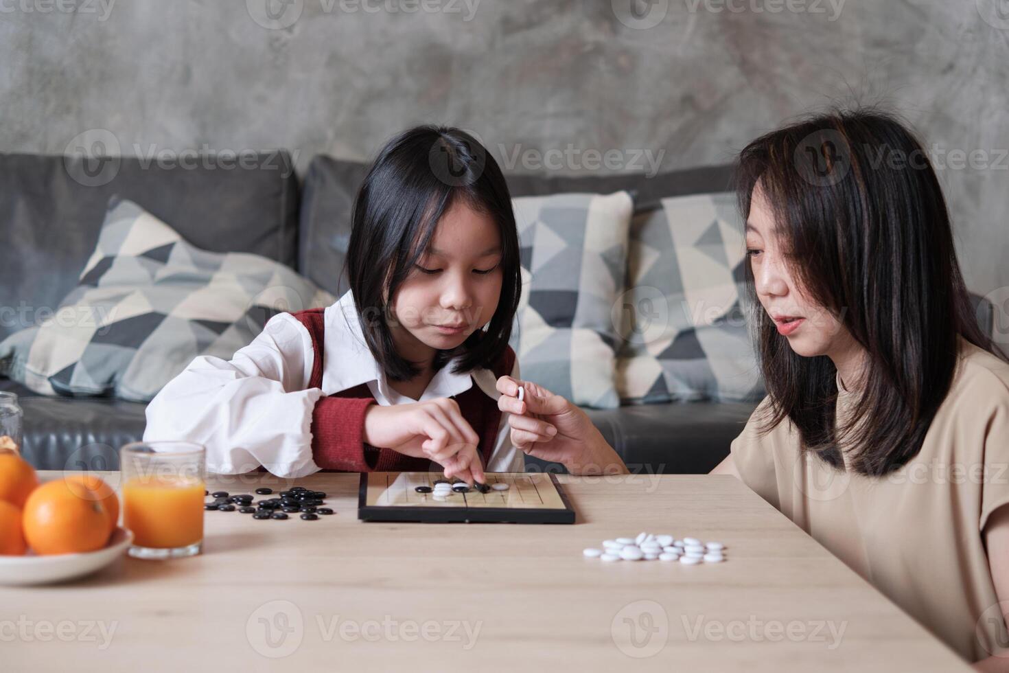 Asian family, mum, and kid fun playing Go, checkers board game on table at living room together with love and cheerful, happy weekend relaxing hobby of child and parent, concentrate and compete. photo
