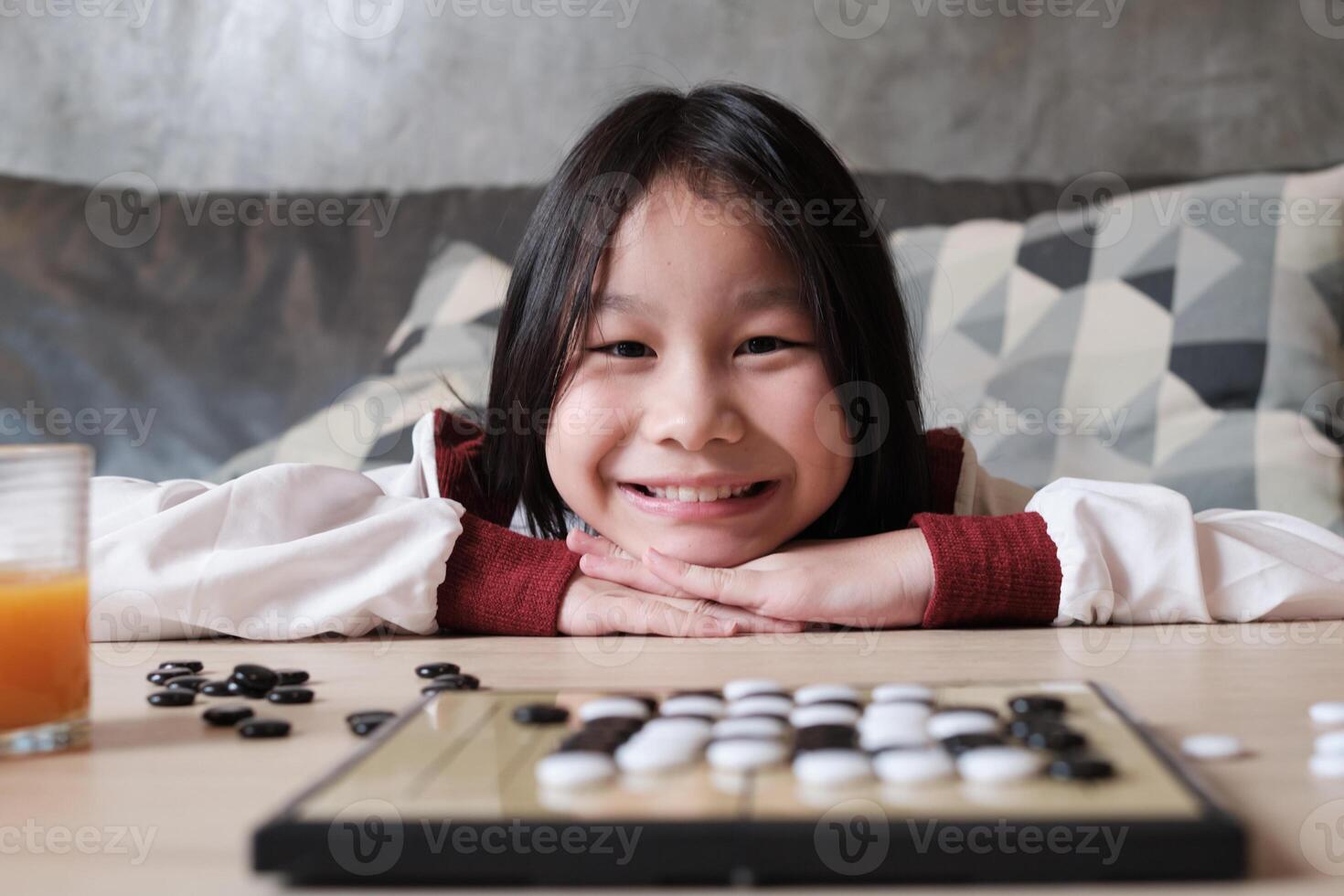 Portrait Close-up shot, one Asian girl fun playing Go, checkers board game on table in home living room, cheerful smile and looking at camera, happy weekend relaxing hobby of clever cute child winner. photo