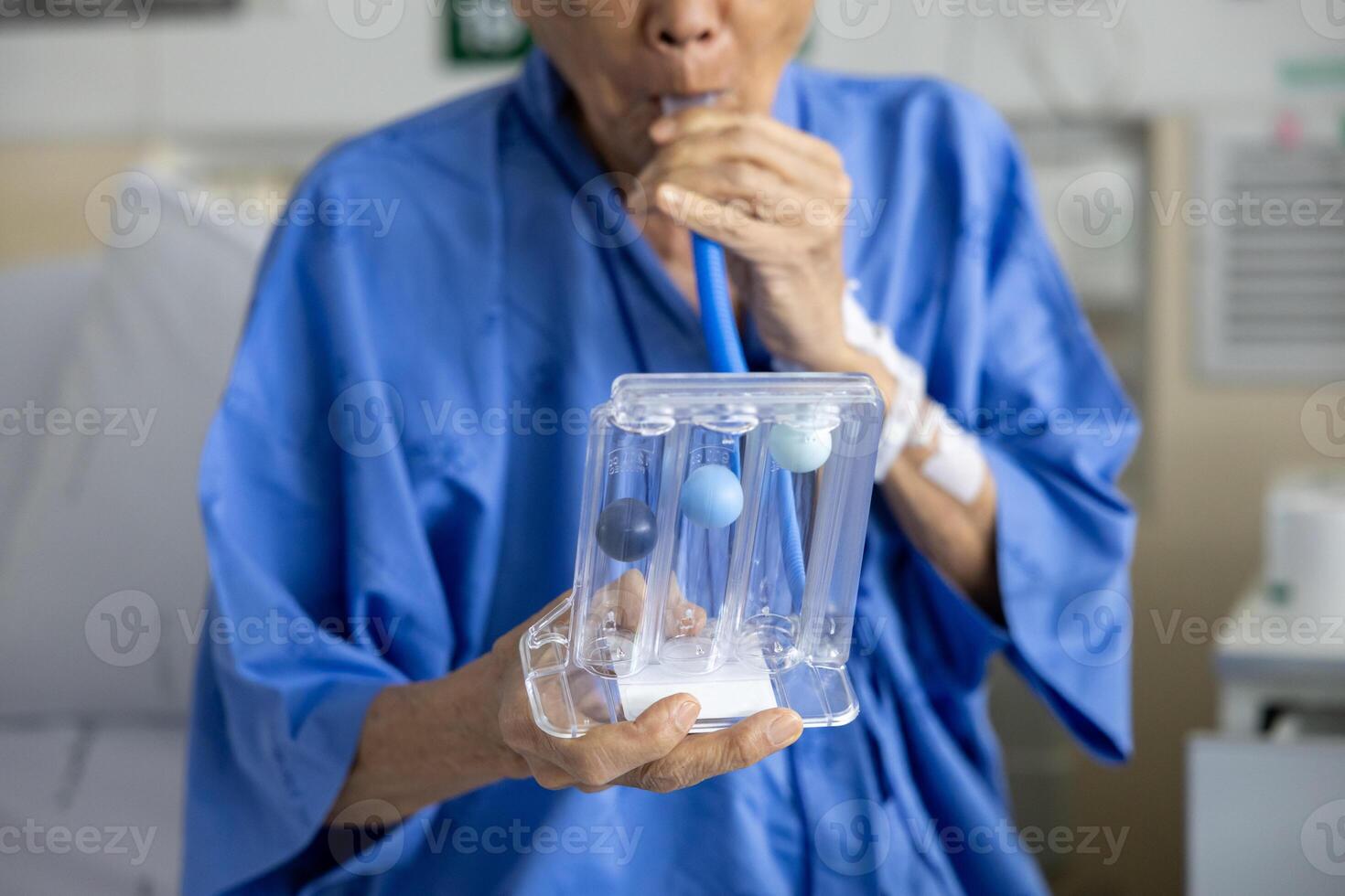 Senior man using incentive spirometer device for breathing exercise rehabilitation to recover from lung cancer after surgery due to heavy smoking in hospital bed photo