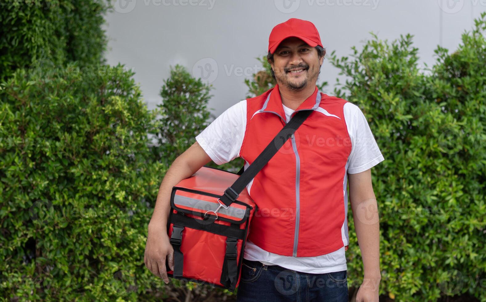 Smiling delivery employee man in red cap t-shirt uniform thermal food bag backpack work courier service photo