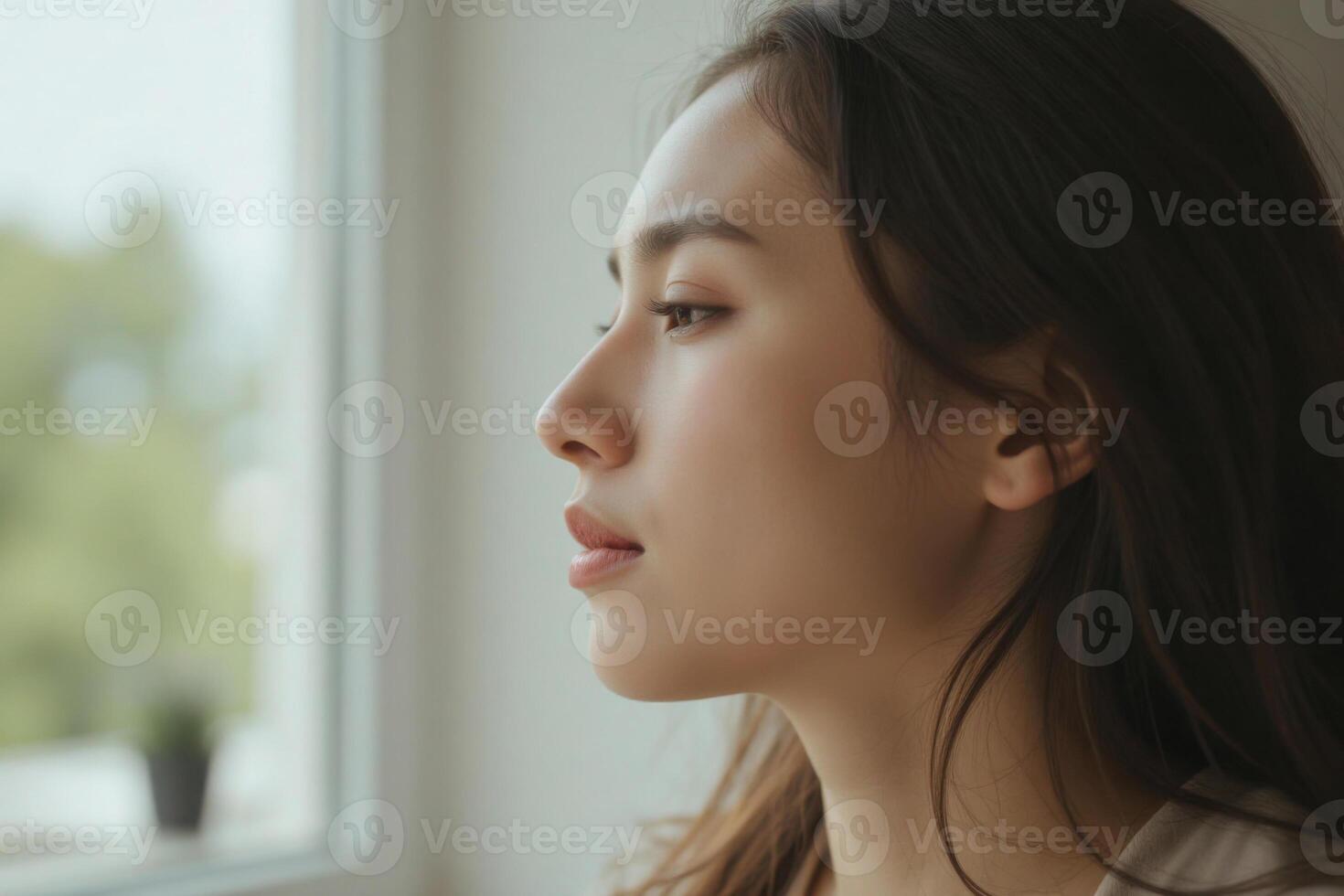 a woman with long, dark hair looking out of a window. The background is blurred photo