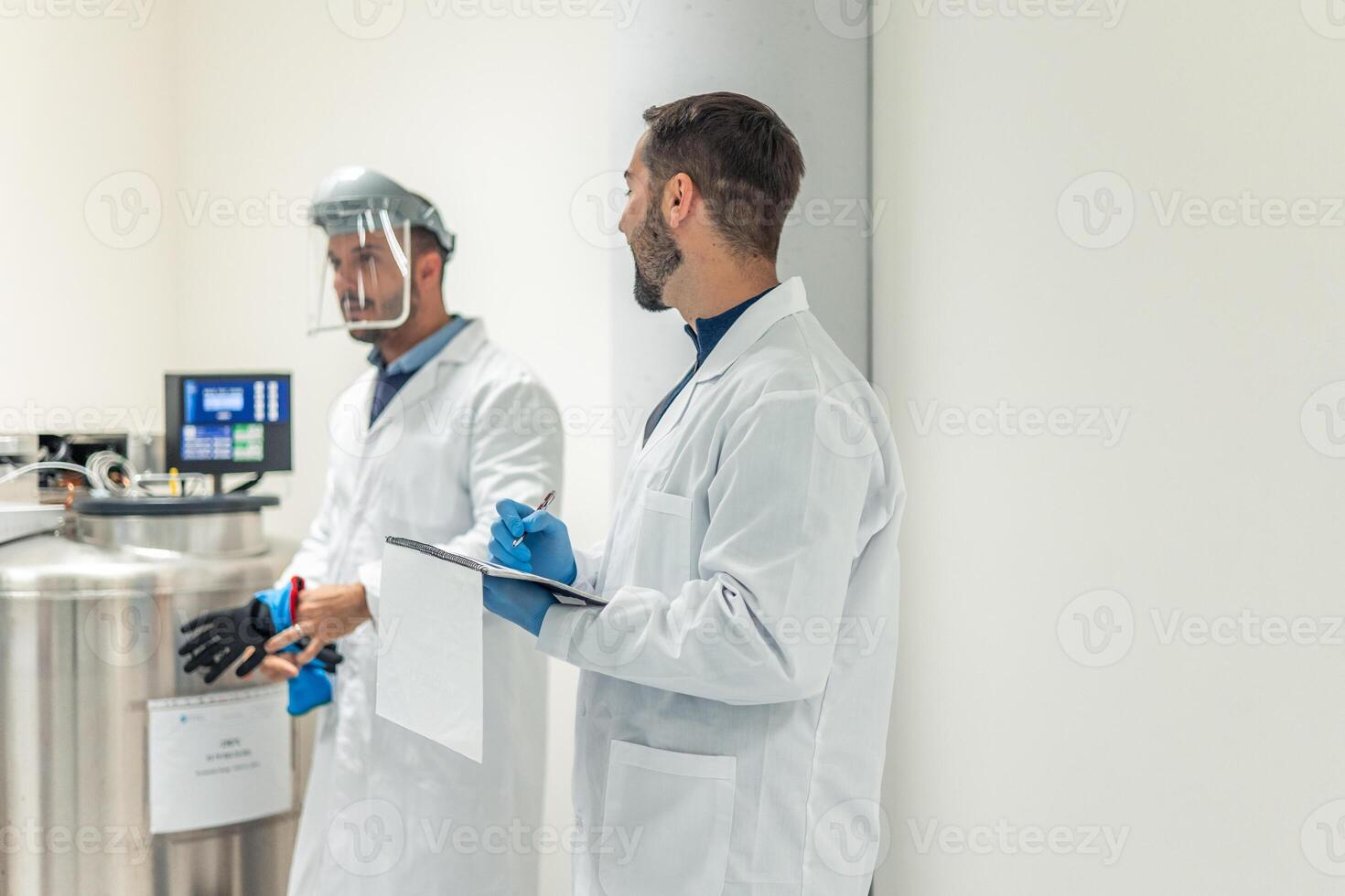 Scientists taking notes and working with cryogenic equipment in laboratory photo