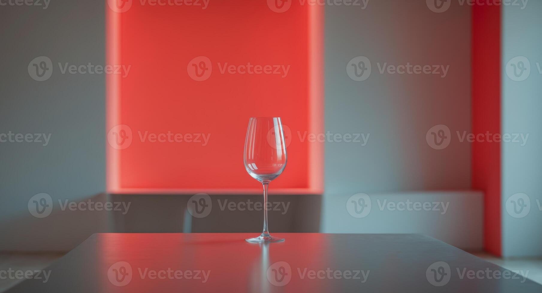 A wine glass is sitting on a table in front of a red wall. photo