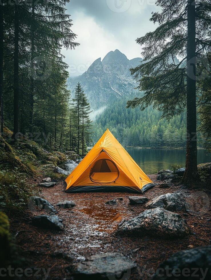 A vibrant yellow tent by a serene lake, surrounded by lush forests and mountains. photo