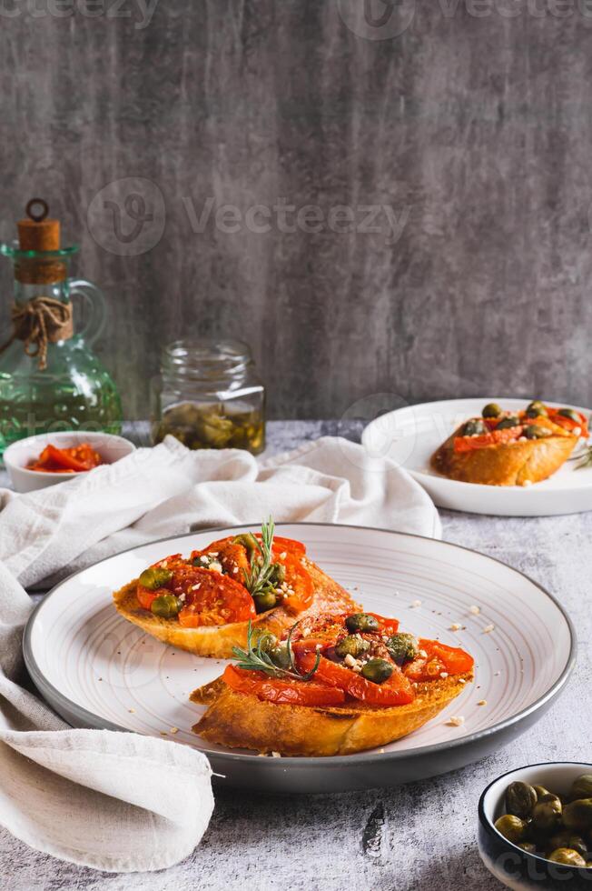 Appetizing bruschetta with dried tomatoes and pickled capers on a plate on the table vertical view photo