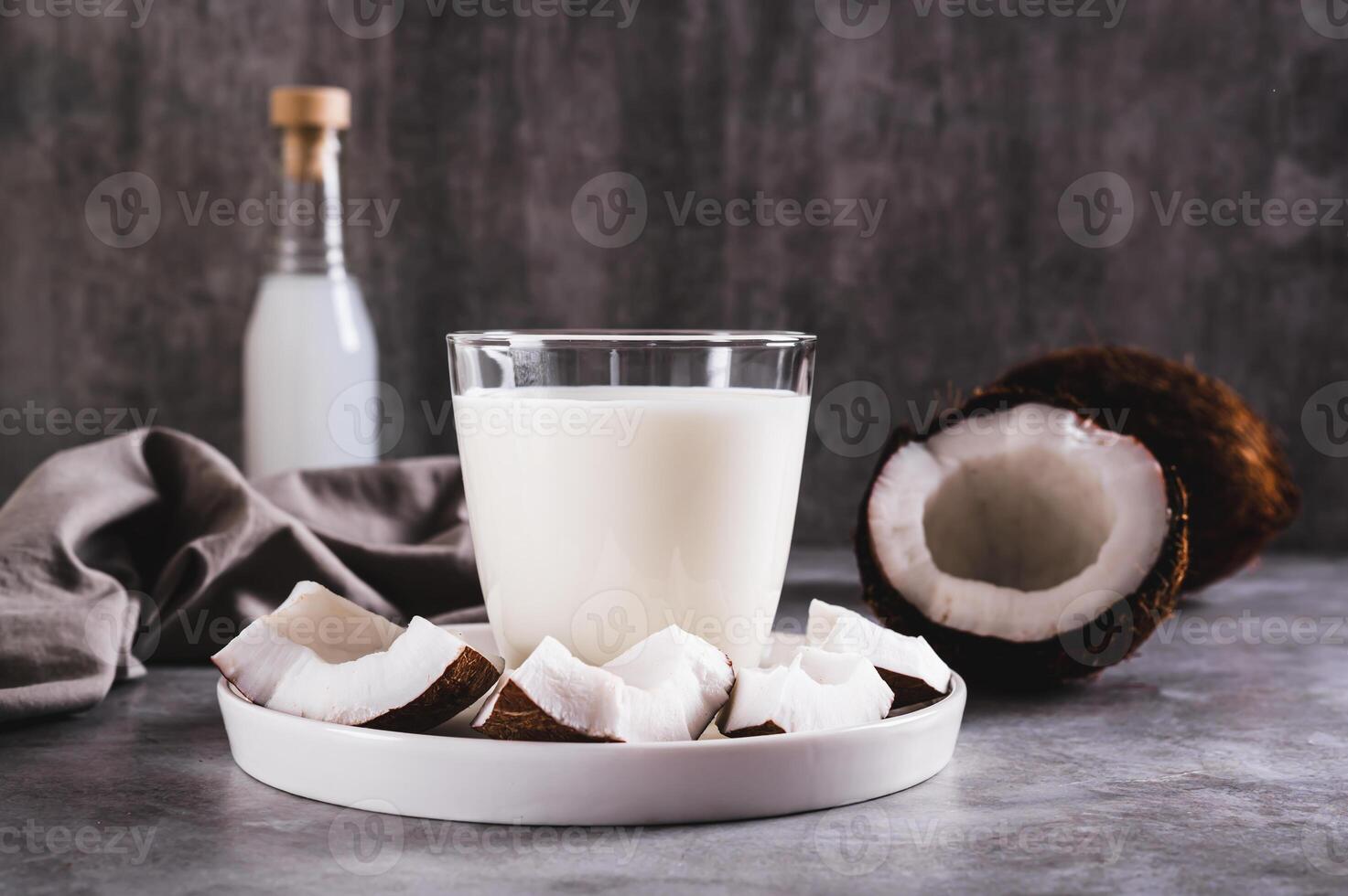 Fresh coconut milk in a glass and coconut pieces on a plate on the table photo