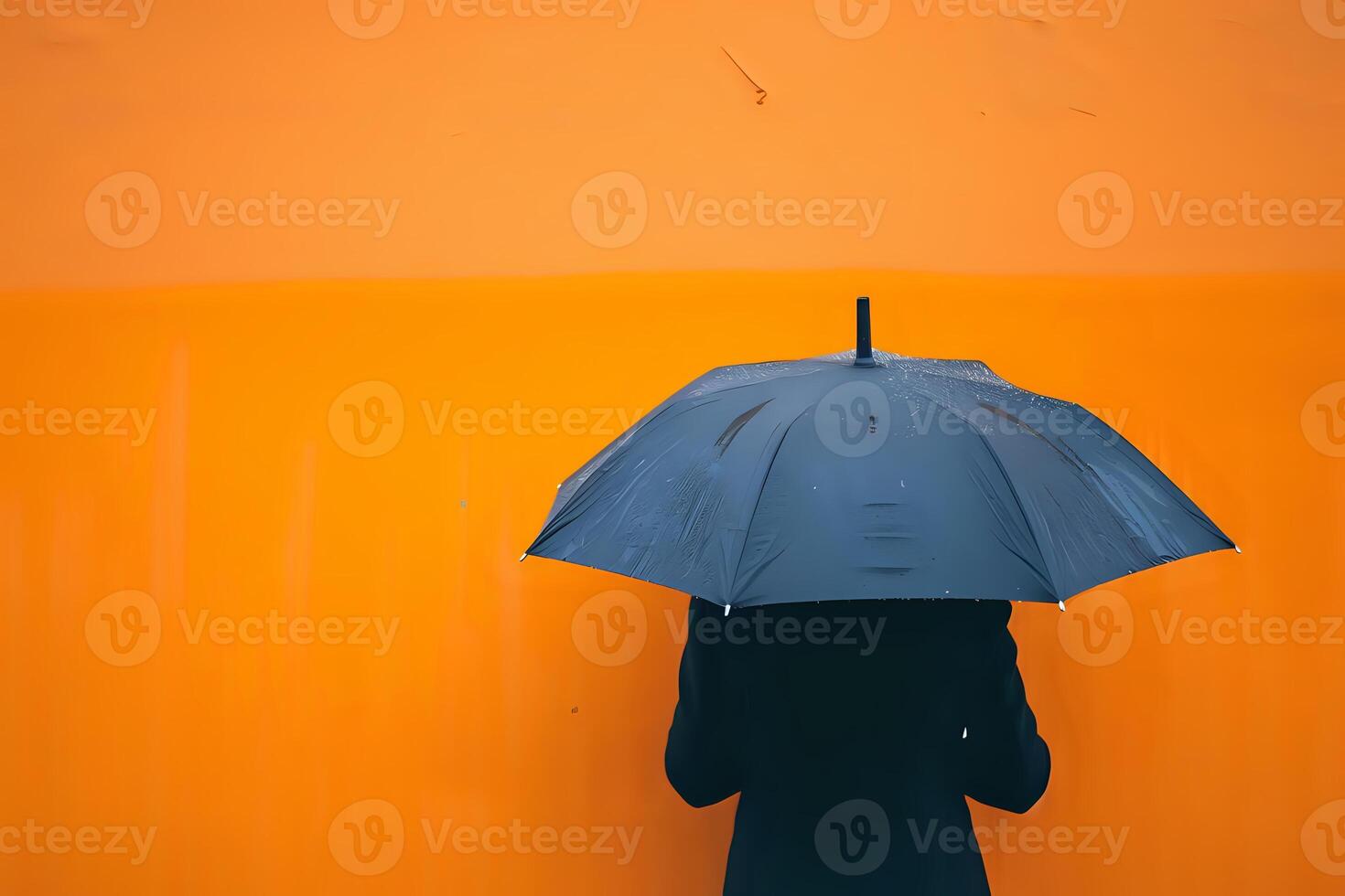 A Person Holds a Black Umbrella Against an Orange Wall During a Rainy Day, Showing Minimalist Street Photography Aesthetics, Featuring a Monochromatic Color Scheme and Striking Contrast photo