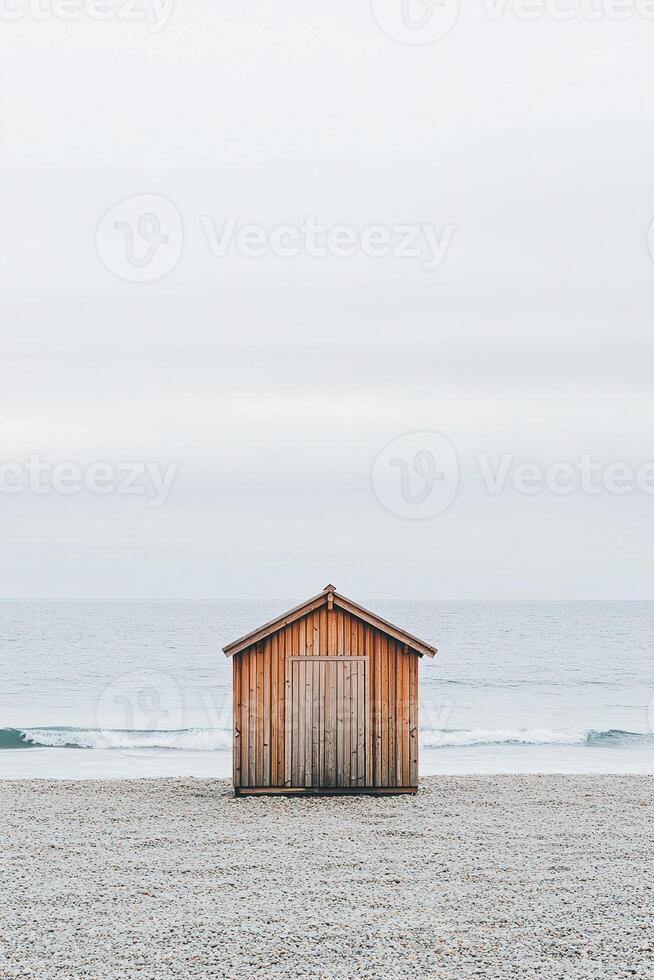 In a tranquil setting, a small wooden beach hut stands on a smooth sandy beach, surrounded by gentle waves and a soft, overcast sky. The atmosphere is peaceful and modern photo