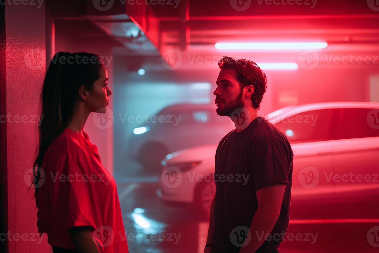 Couple in a dimly lit parking garage sharing an intimate moment under neon red lights during the evening hours photo