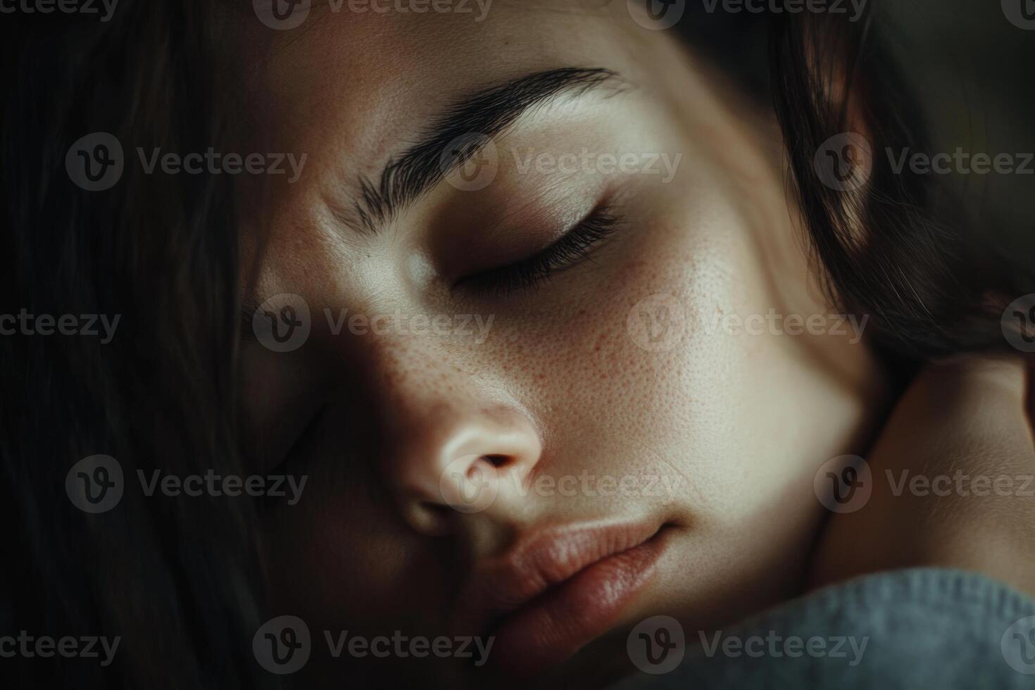 A young woman rests peacefully with her eyes closed, captured in soft light, conveying tranquility and relaxation in an intimate setting photo