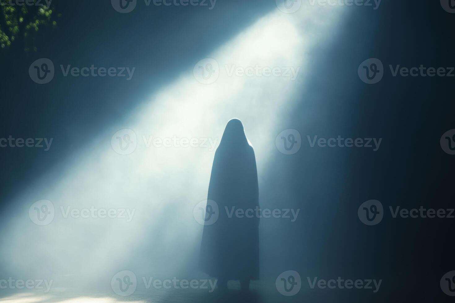 A person in a hood standing in the dark with light coming from the top photo