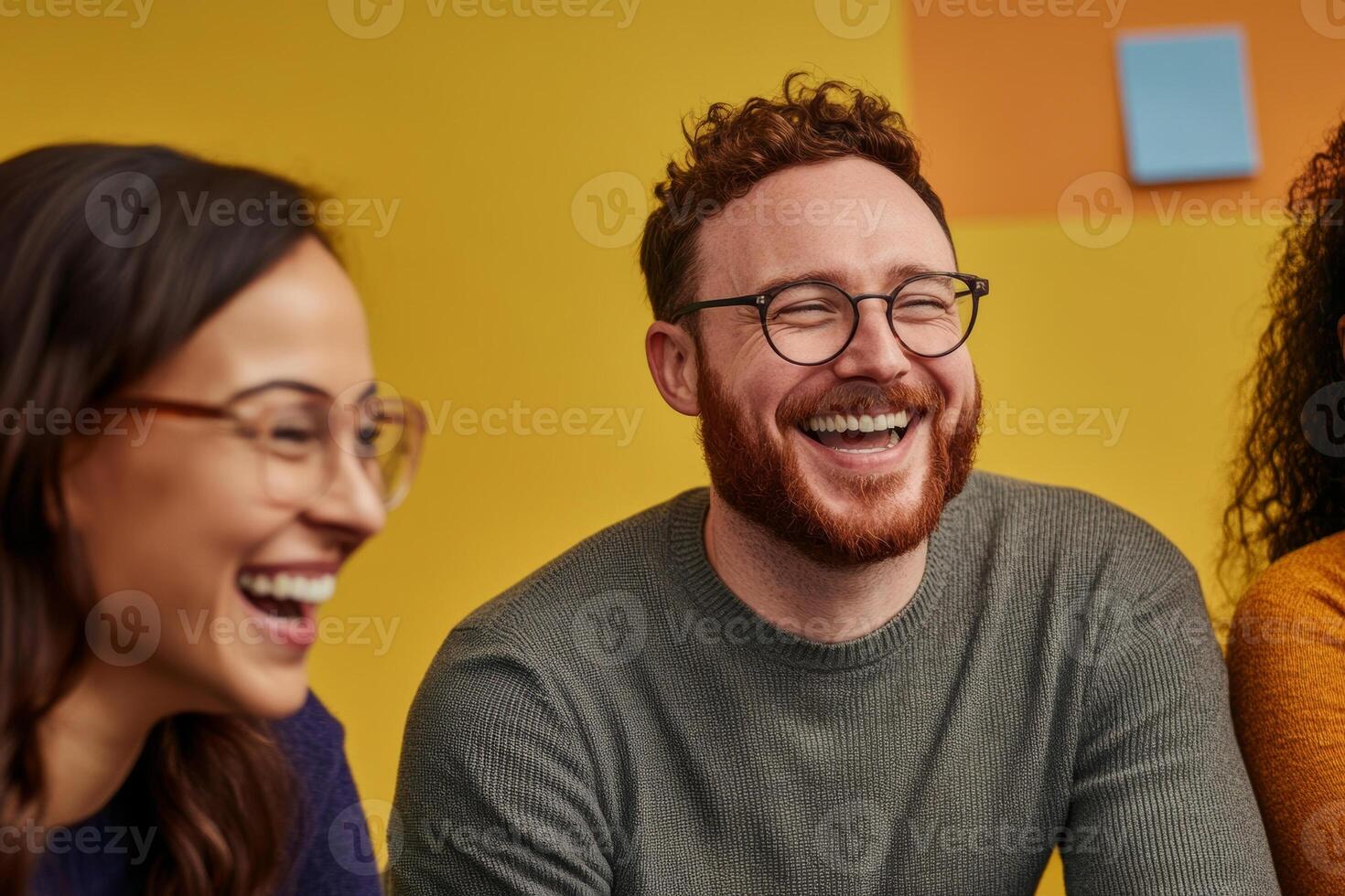 Three people laughing and smiling in front of a yellow wall photo