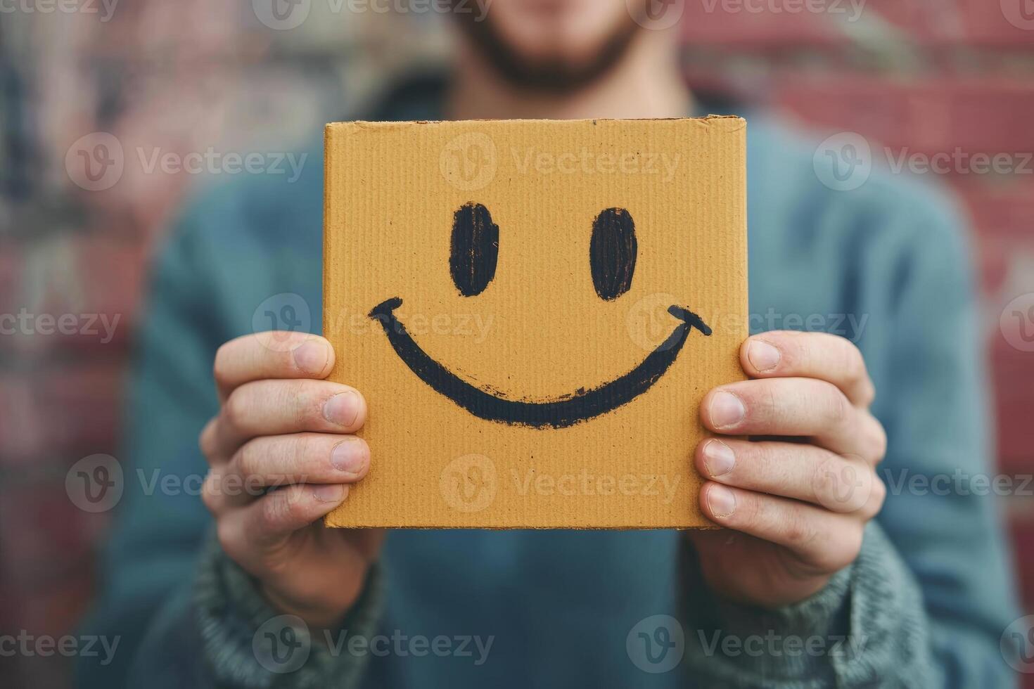 Person holding a cheerful box with a smiley face against a textured brick wall during daylight photo