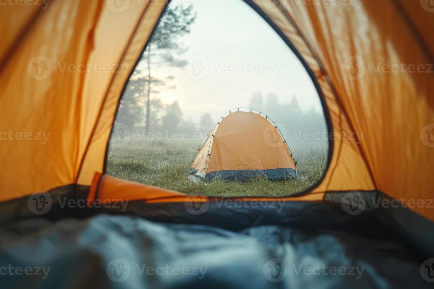A peaceful morning view from a tent showcasing a foggy campsite with a second tent in the background surrounded by serene nature photo
