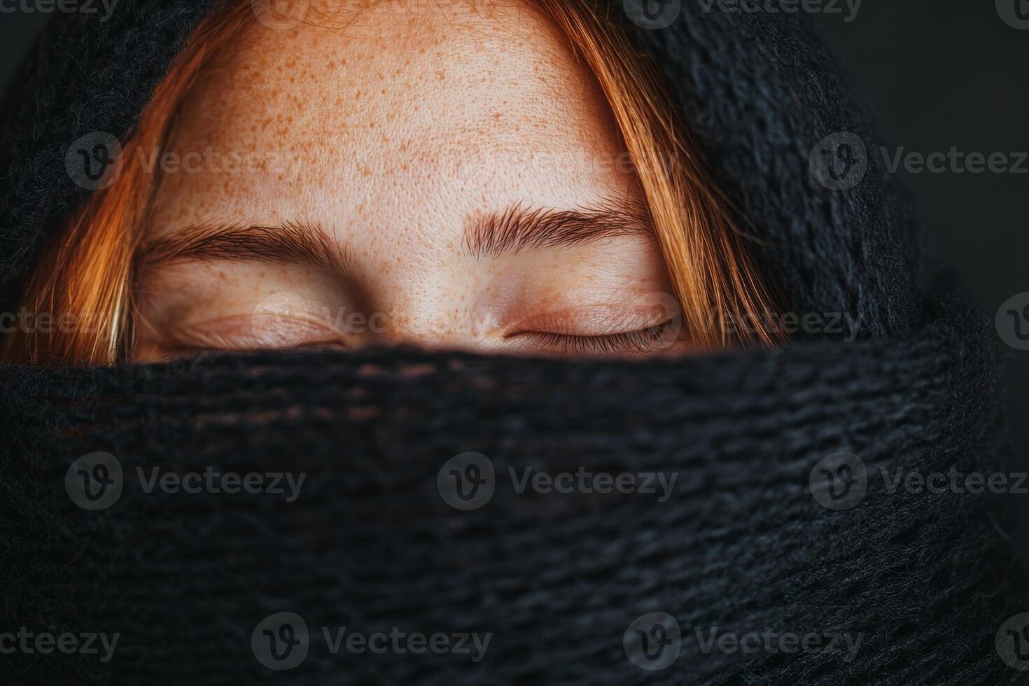 A woman with freckled skin and red hair is wrapped in a black shawl, eyes closed in peaceful contemplation against a dark background photo
