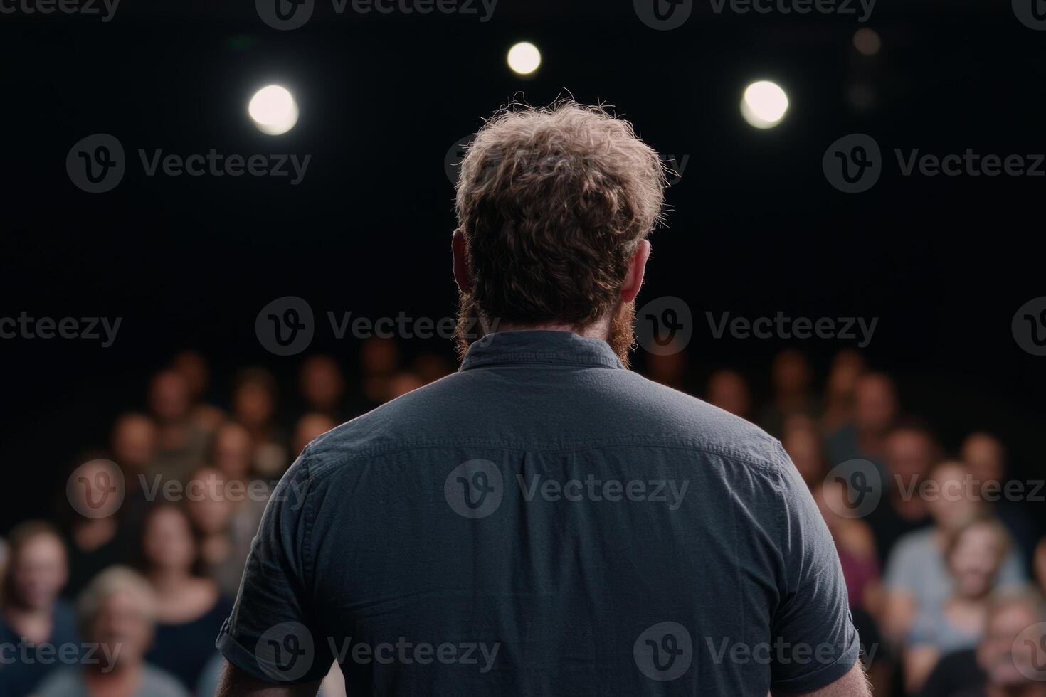 A speaker engages an audience during an event in a dimly lit auditorium filled with attentive listeners photo
