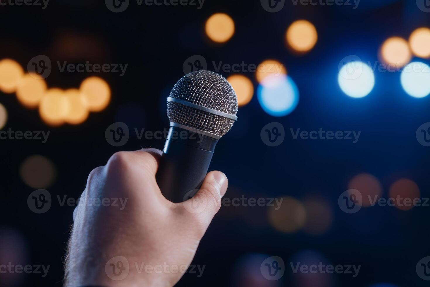 A hand holding a microphone in a dimly lit venue with bright lights during a live performance or speech event photo