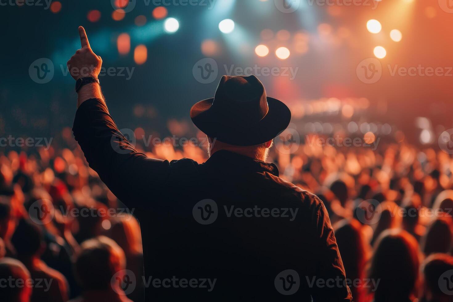 A concertgoer raises a hand with enthusiasm during a live music performance at a vibrant venue filled with cheering fans photo