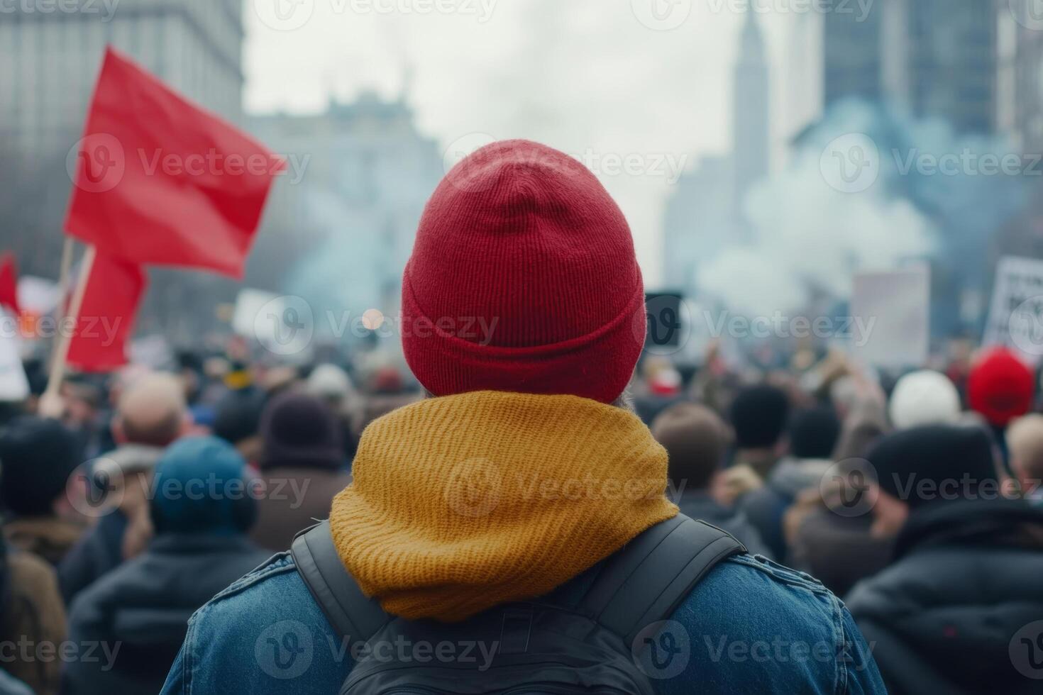 A person in a red beanie and yellow scarf stands amidst a crowd at a protest in a city with flags and smoke, capturing the spirit of activism photo
