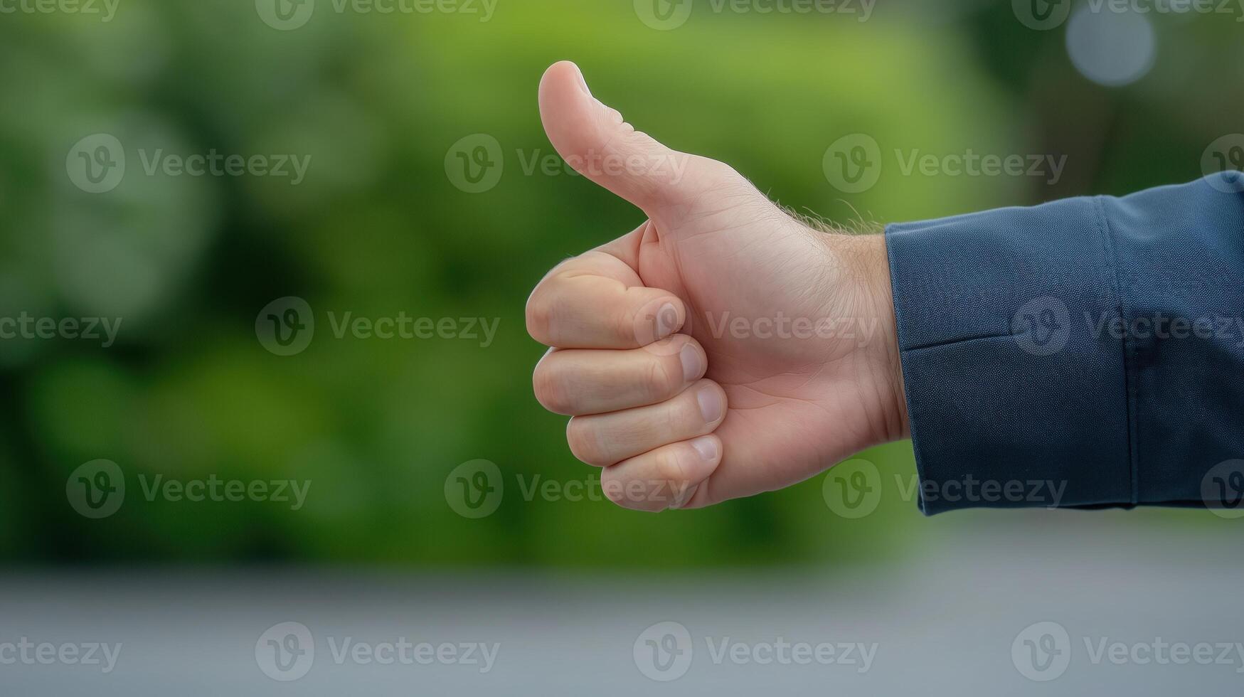 Hand Giving Thumbs Up Gesture Outdoors Showing Approval, Focus on Right Hand Against Blurred Green Background, Wearing Dark Jacket, Symbolizing Positive Feedback, Agreement, Supportive Gesture photo