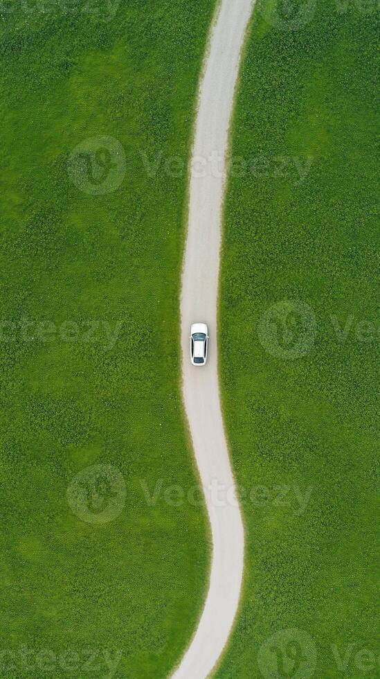 Aerial View of Car Driving on Winding Road Through Vast Green Landscape Expressing Tranquility and Freedom photo