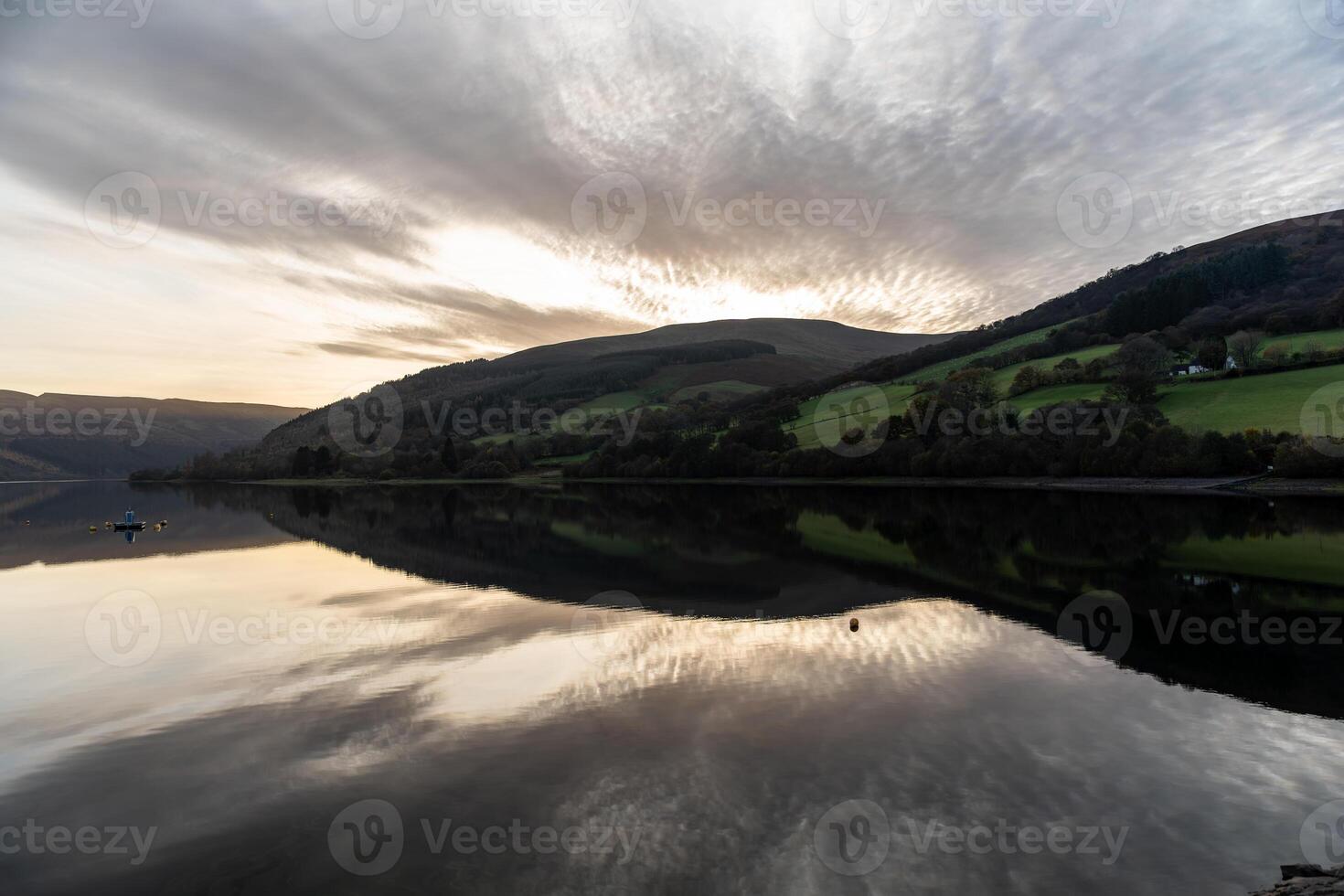 Calm lake reflecting green hills and cloudy sky at sunset photo