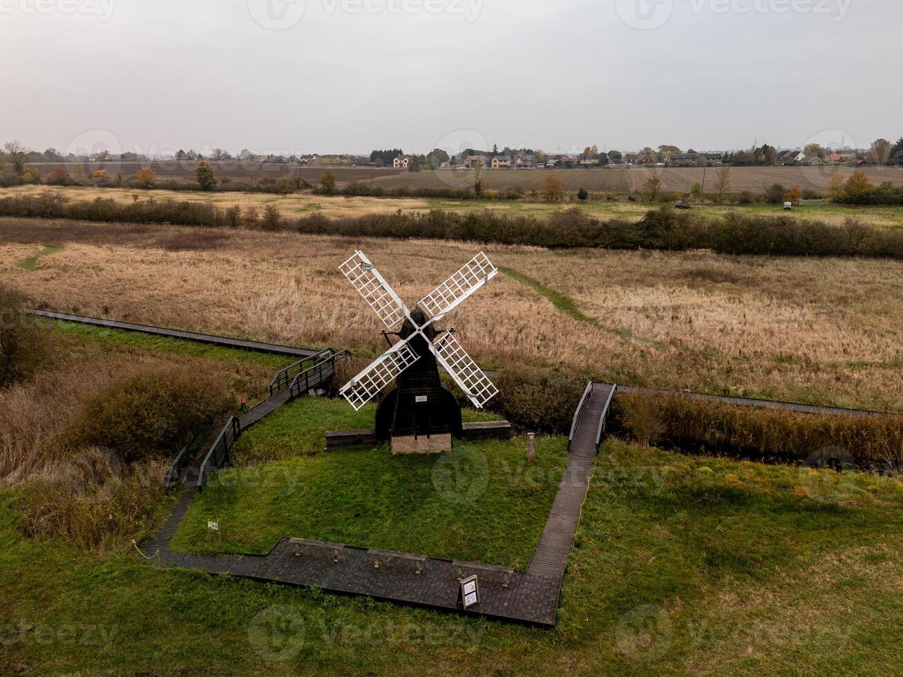 Traditional windmill stands in green field, captured from above on cloudy day photo