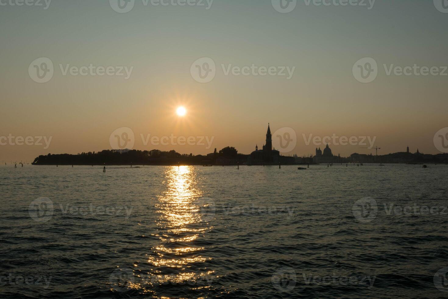 Sun setting on the horizon, creating a golden path on the sea in venice photo