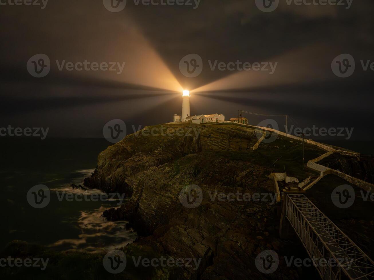 Powerful lighthouse illuminating the dark night on a cliff overlooking the ocean photo