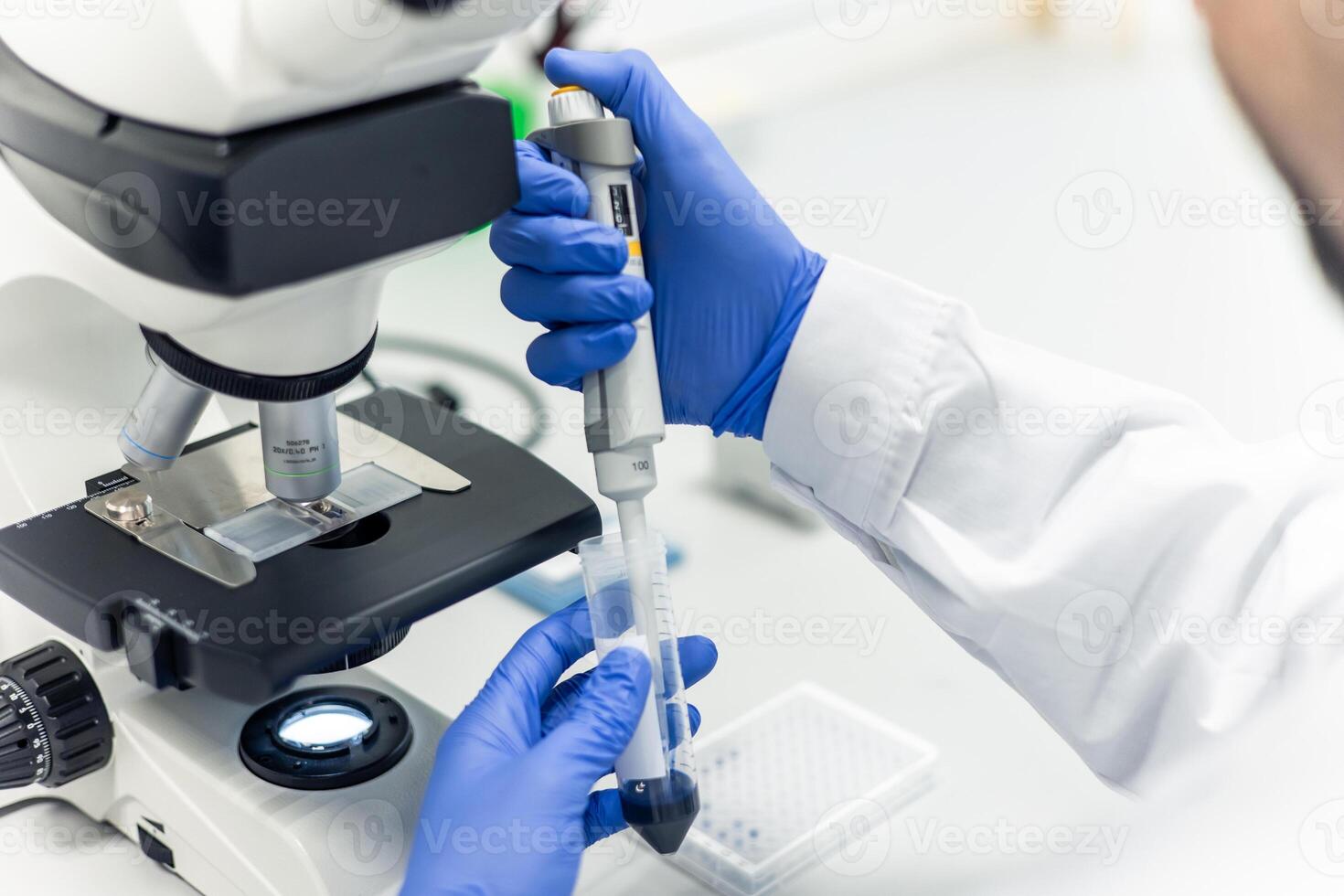Scientist using micropipette and microscope during scientific experiment in laboratory photo