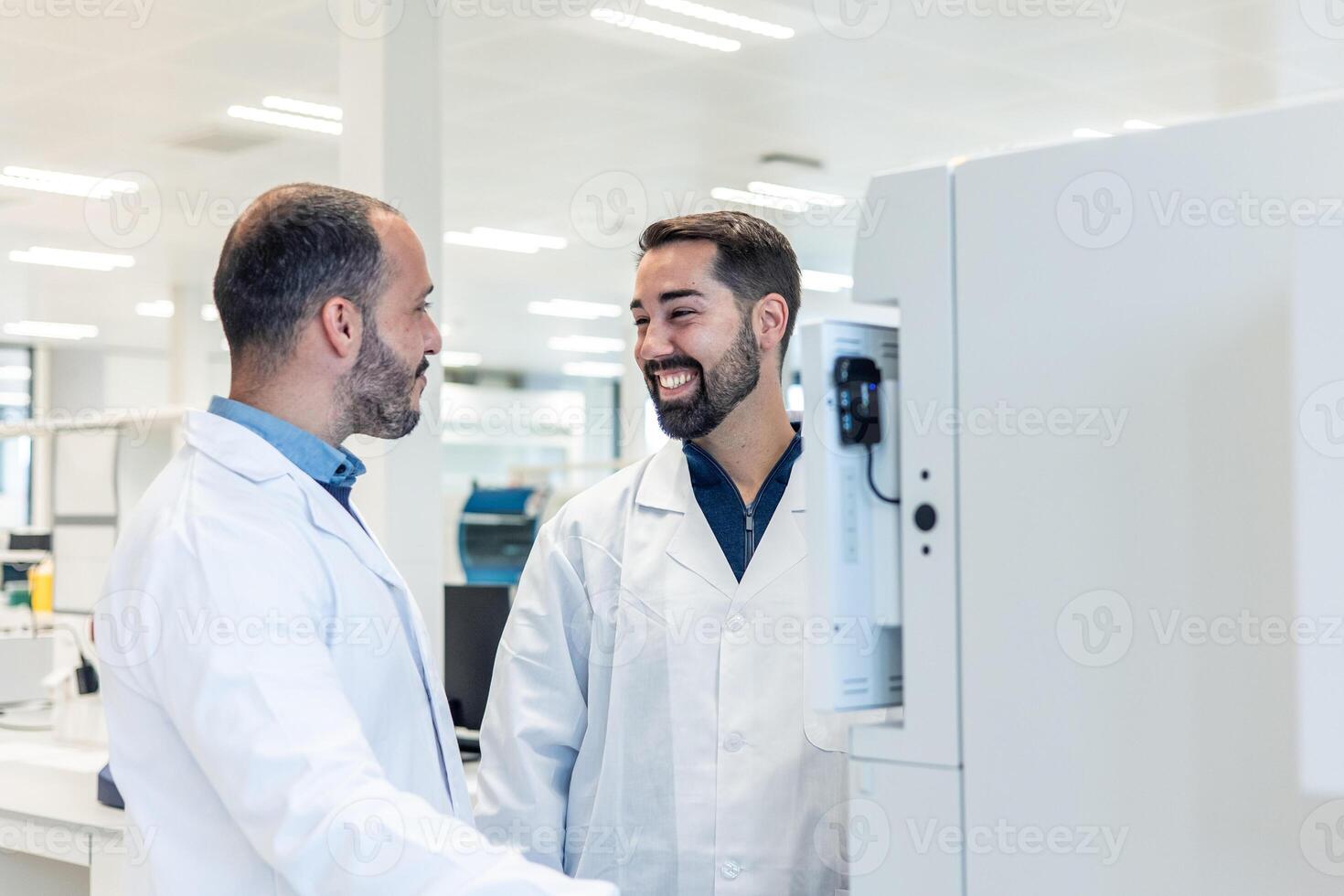 Two smiling scientists discussing next to a machine in laboratory photo