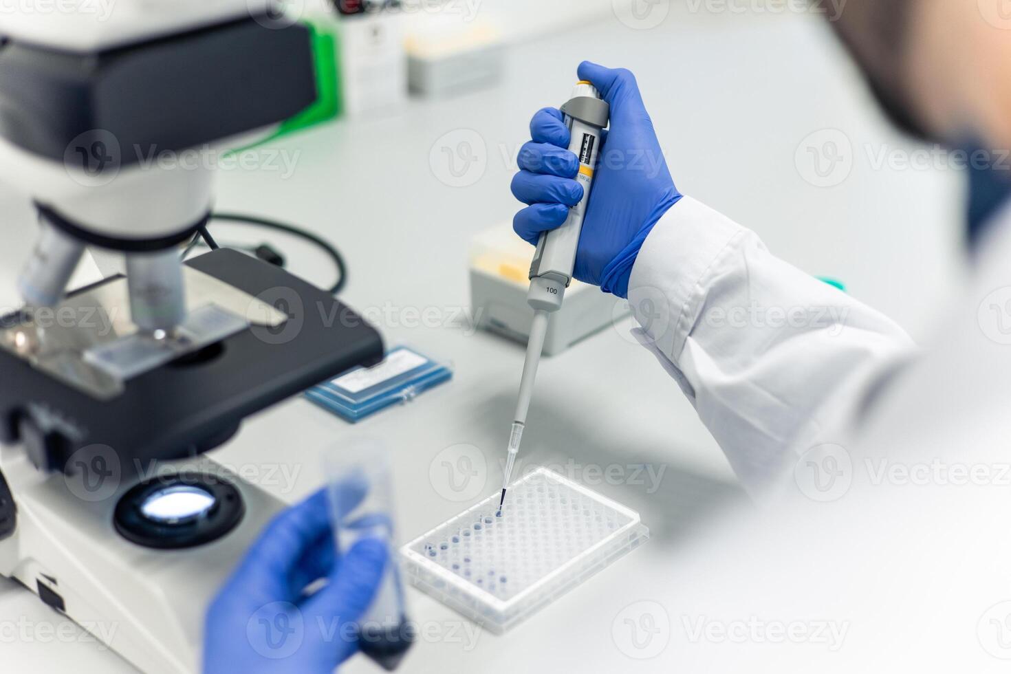 Scientist using micropipette and microplate near microscope in laboratory photo