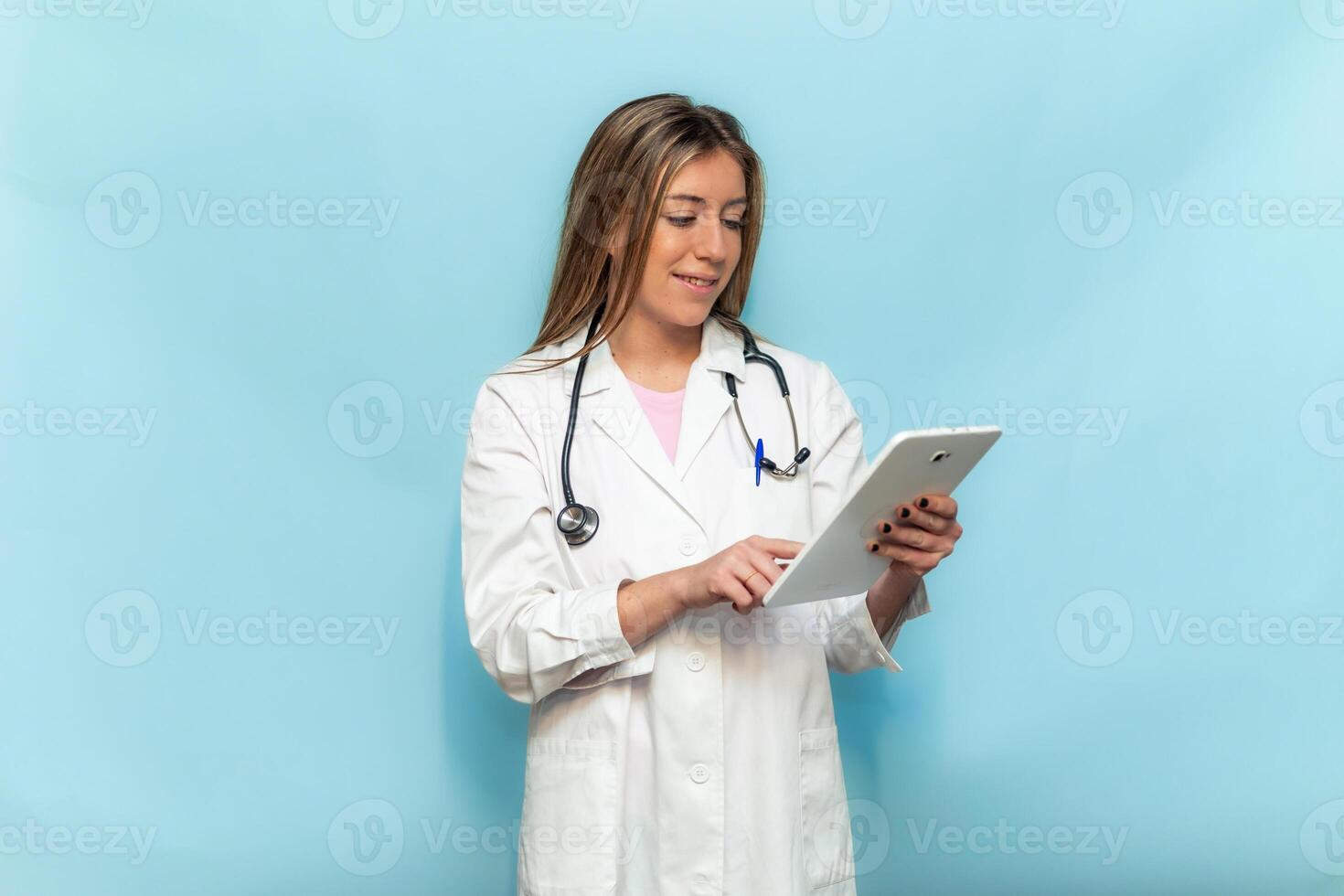 Female doctor wearing lab coat and stethoscope using tablet on light blue background photo