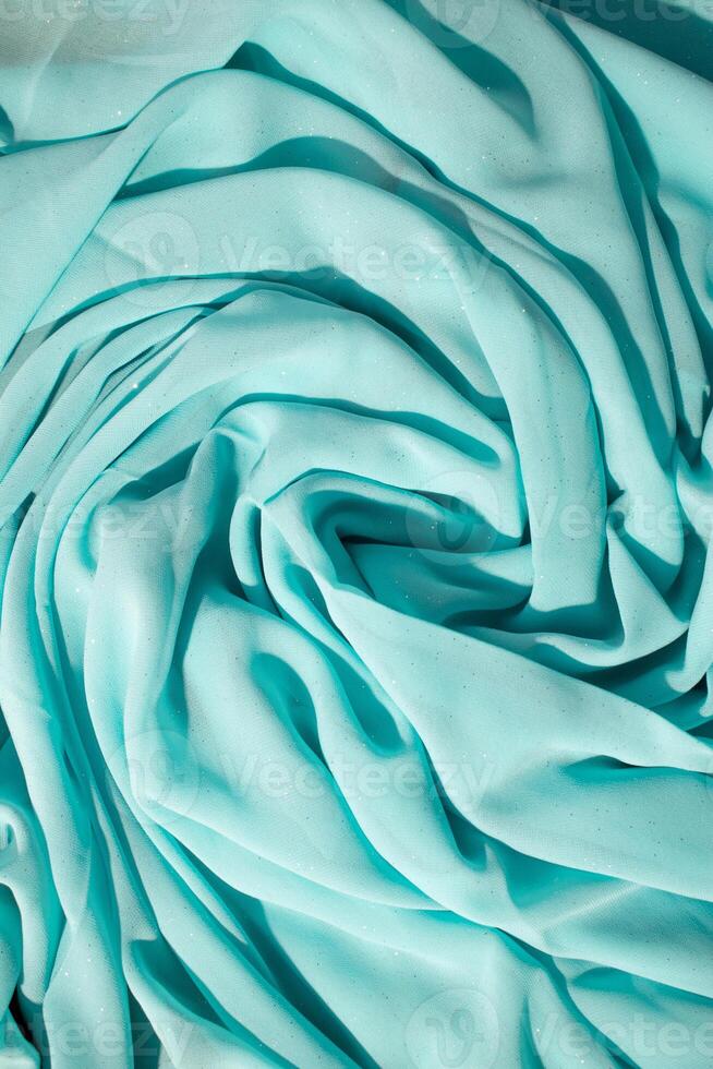 Spiral Twisted Turquoise wavy crumpled fabric with little sparkling dust, texture and background. photo