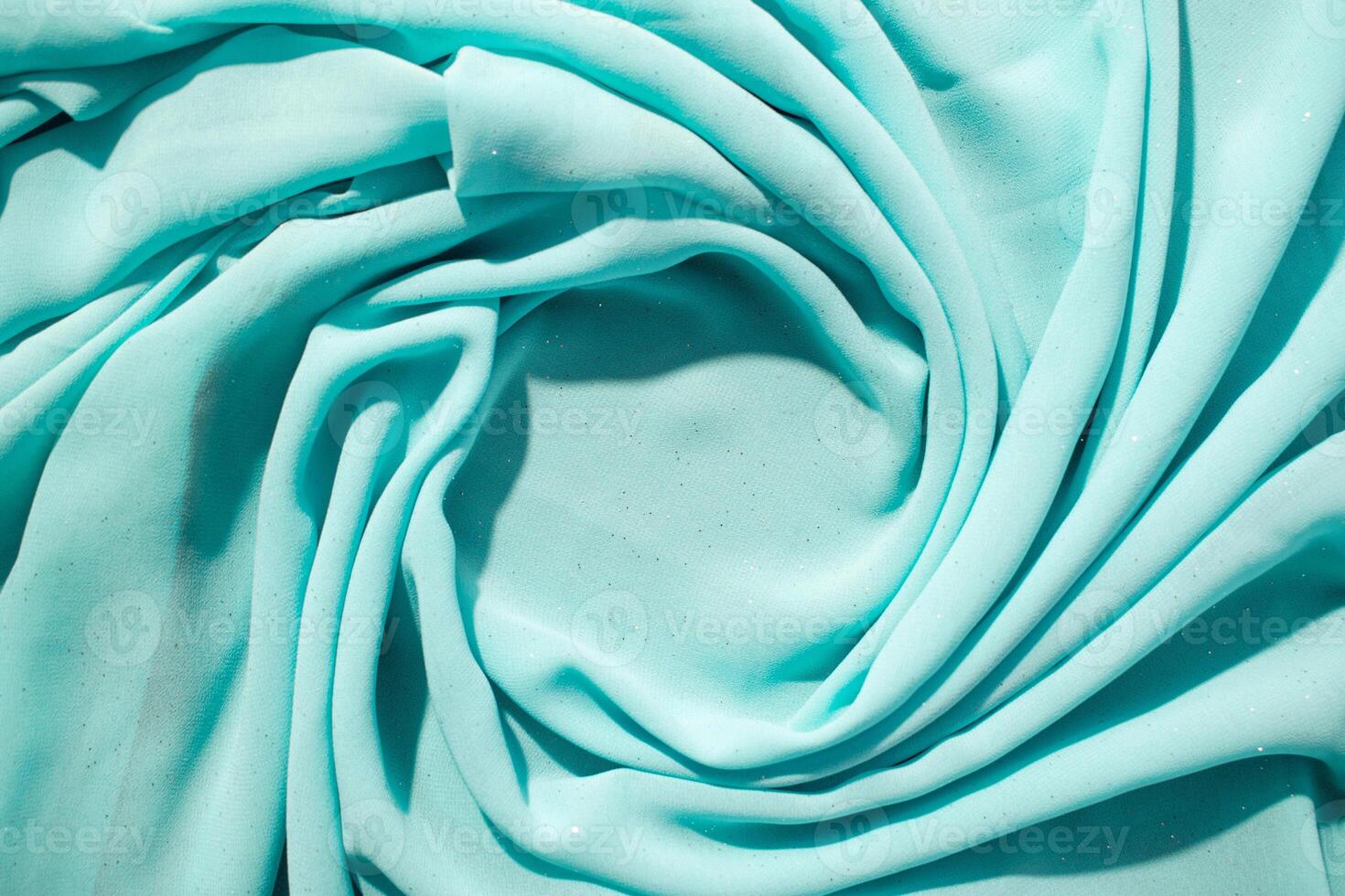 Spiral Twisted Turquoise wavy crumpled fabric with little sparkling dust and copy space in center, abstract background. photo