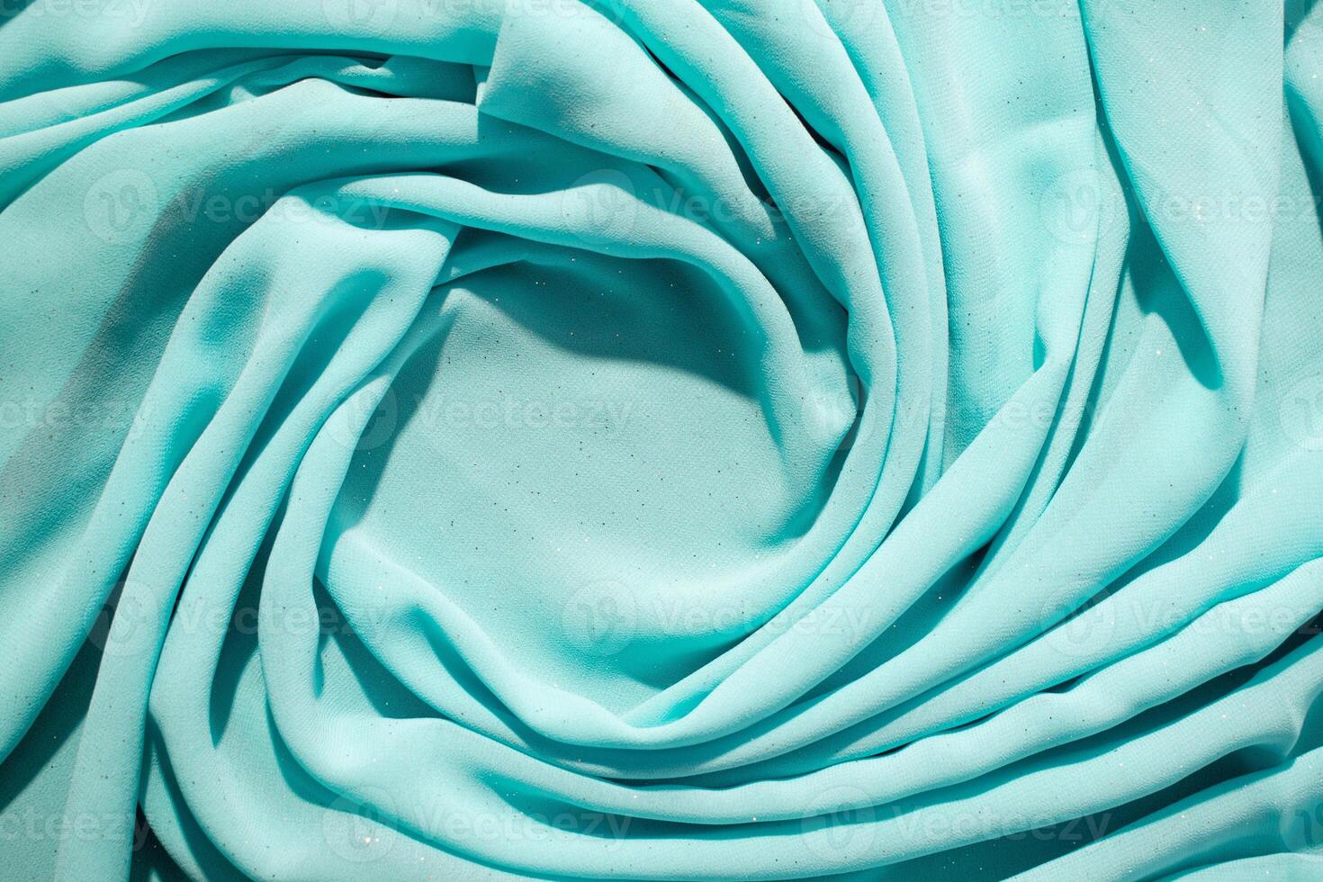 Spiral Twisted Turquoise wavy crumpled fabric with little sparkling dust and copy space in center, abstract fabric background. photo