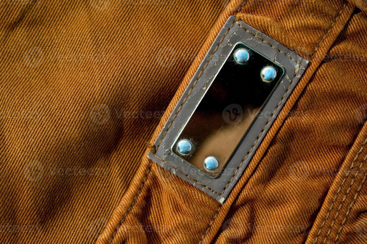 Blank shiny metallic label on bright brown jeans, fabric texture mockup photo