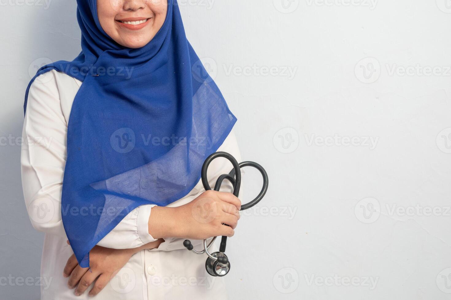 Cheerful Muslim Female asian doctor or nurse standing and holding stethoscope with copy space. Isolated white background. Medical, healthcare and nurse concept. photo