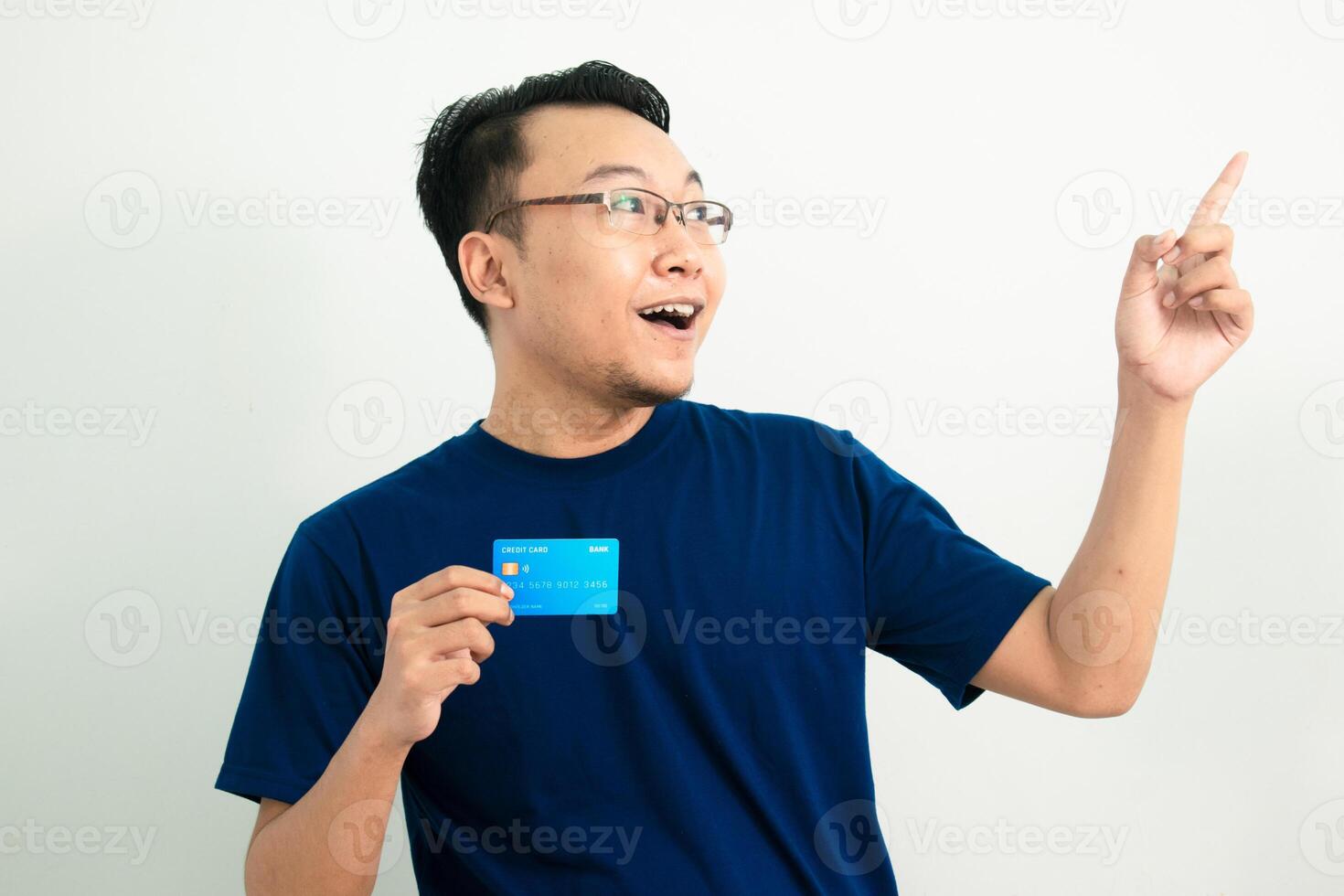 Cheerful asian man hold credit card with pointing pose. Banking, Financial isolated background, blue color concept. photo