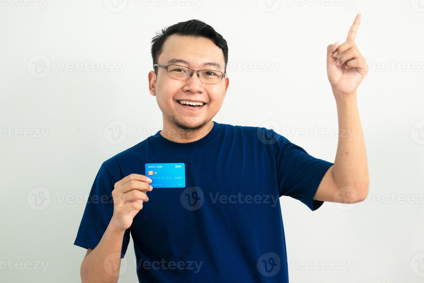 Delighted asian man hold credit card with pointing pose. Banking, Financial isolated background, blue color concept. photo