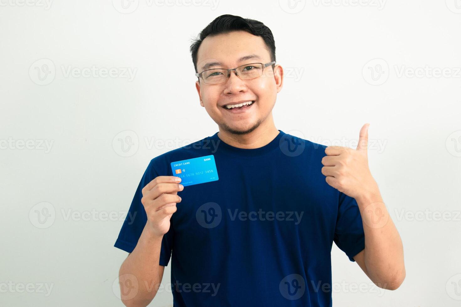 Happy asian man hold credit card with thumb up pose. Banking, Financial isolated background, blue color concept. photo