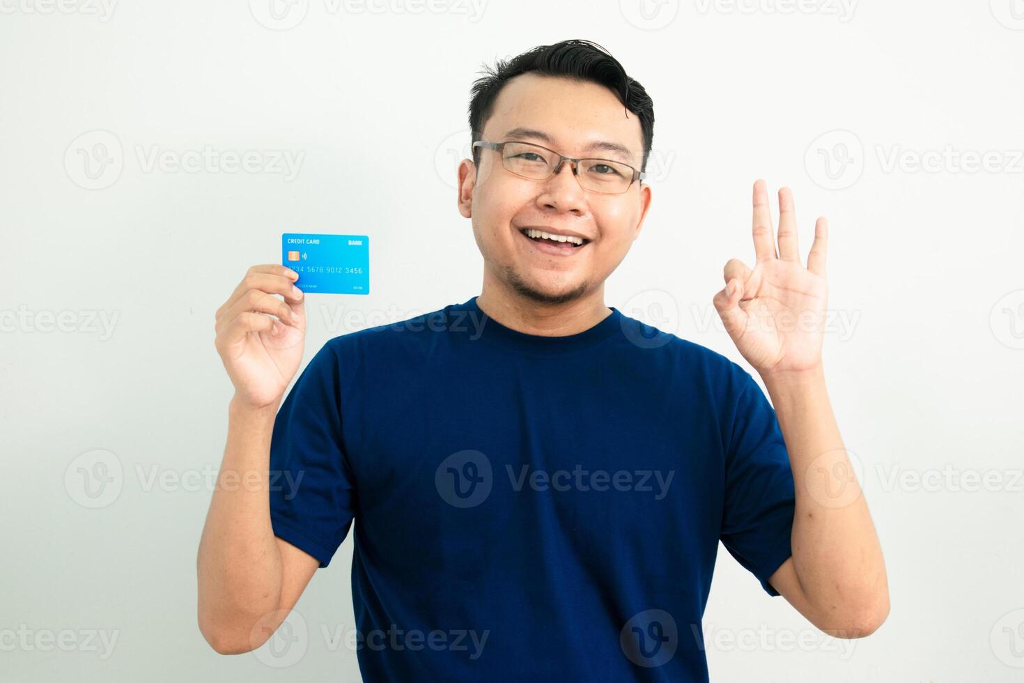 Joyful asian man hold credit card with Ok hand sign pose. Banking, Financial isolated background, blue color concept. photo