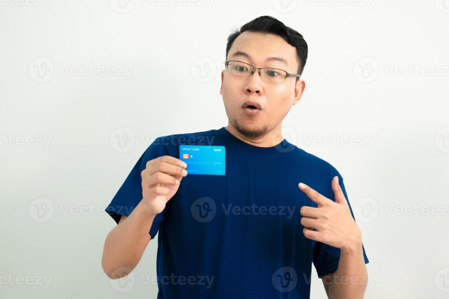 Surprised asian man hold and pointing credit card. Financial isolated background, blue color concept. photo