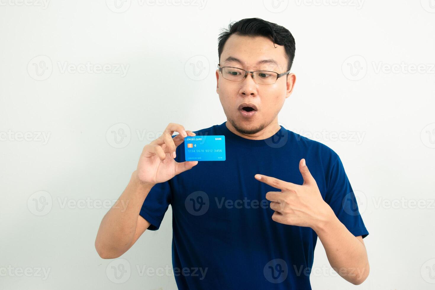 Surprised asian man wear blue tshirt hold and pointing credit card. Financial isolated background, blue color concept. photo